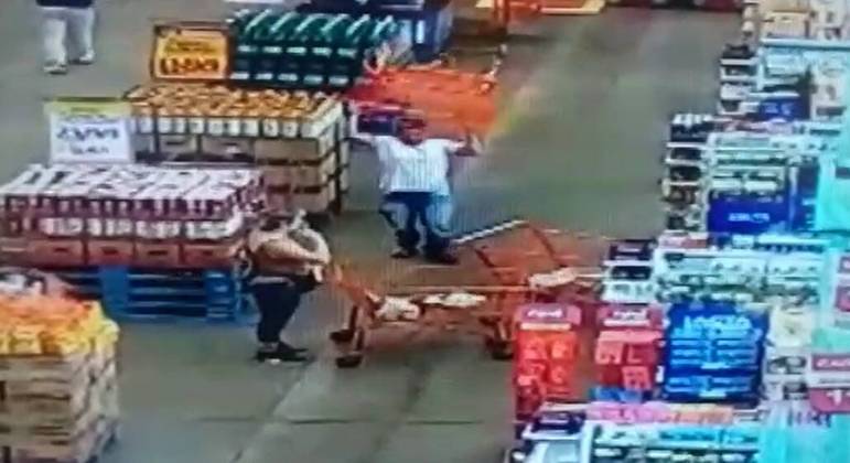  Homem arremessa carrinho de compras em mulher dentro de mercado.